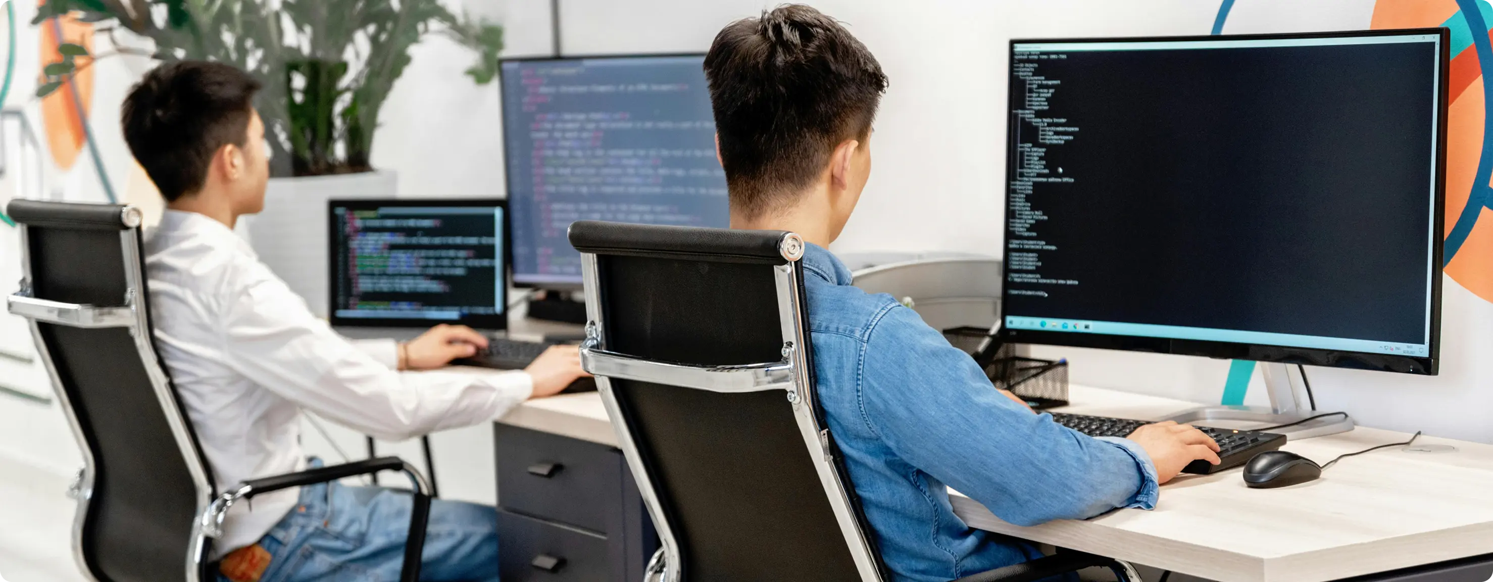 Two men at desks in an office environment, each operating a computer and involved in their work activities.